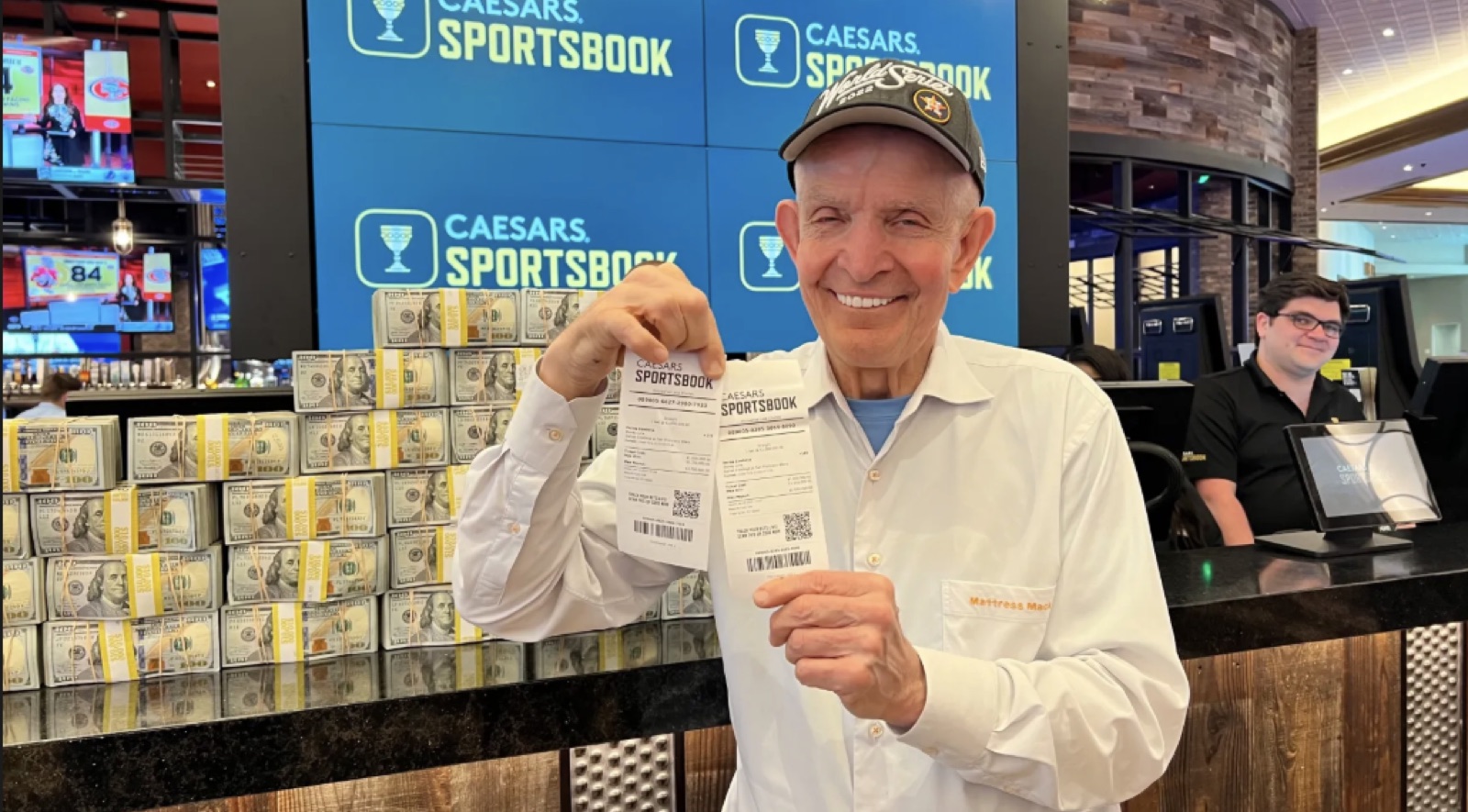 Jim 'Mattress Mack' McIngvale at Caesars Sportsbook, holding betting tickets in front of stacks of cash.